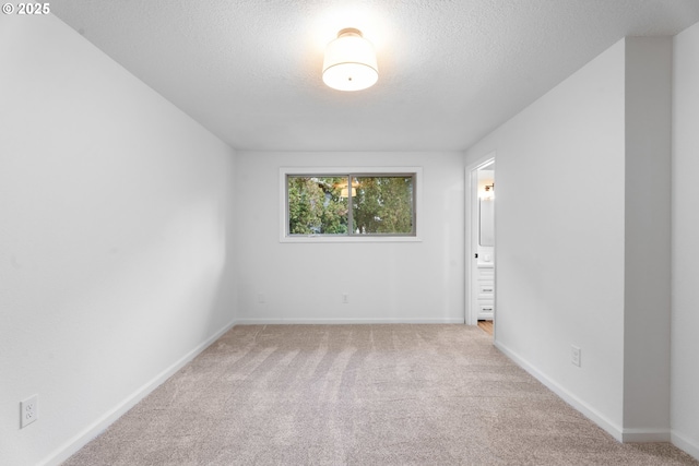 spare room featuring light colored carpet, a textured ceiling, and baseboards