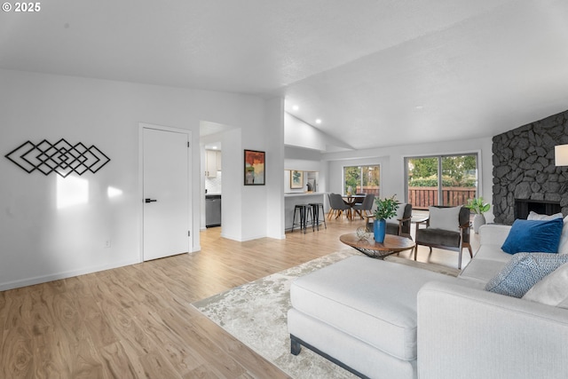 living room with a stone fireplace, lofted ceiling, and light hardwood / wood-style flooring