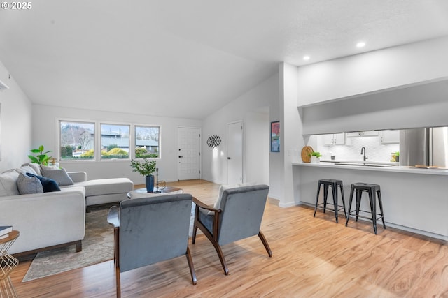 living area with lofted ceiling, light wood finished floors, baseboards, and recessed lighting