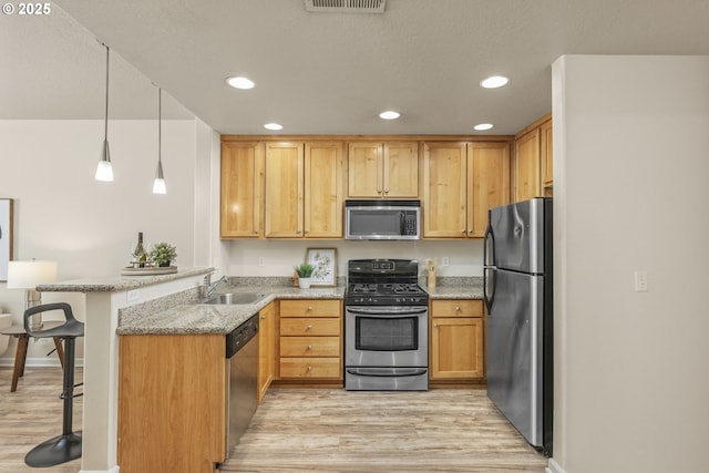 kitchen with a breakfast bar area, light wood-style flooring, appliances with stainless steel finishes, a peninsula, and a sink