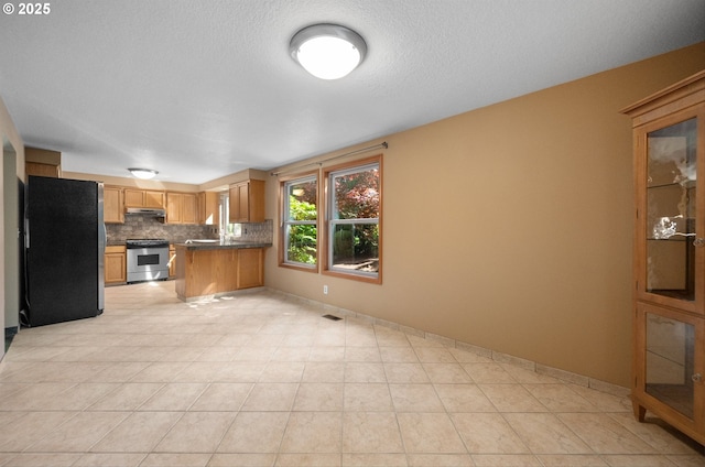 kitchen with dark countertops, stainless steel appliances, backsplash, a peninsula, and under cabinet range hood