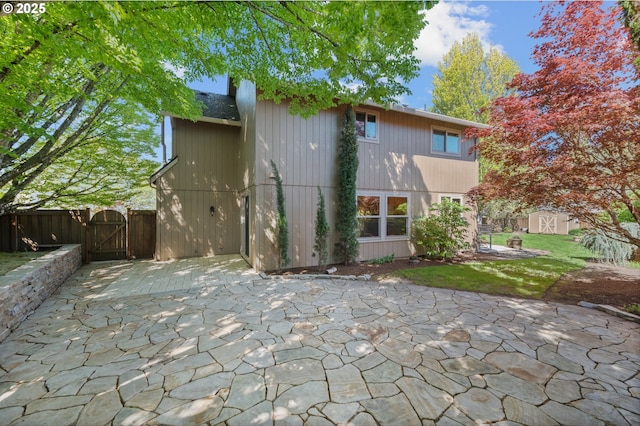 rear view of property with fence, a gate, an outbuilding, a patio area, and a storage shed