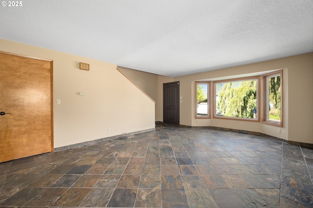 empty room featuring baseboards, stone tile floors, and a textured ceiling