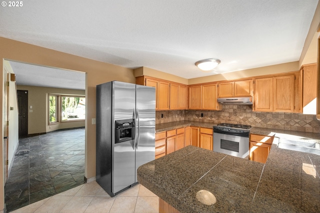 kitchen featuring tile countertops, appliances with stainless steel finishes, tasteful backsplash, a sink, and under cabinet range hood