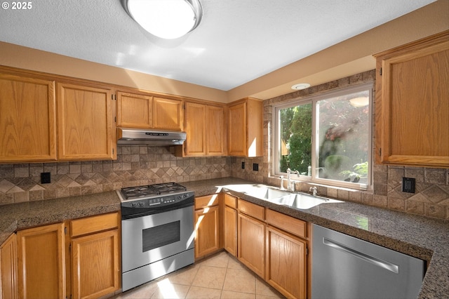 kitchen with appliances with stainless steel finishes, a sink, backsplash, light tile patterned floors, and under cabinet range hood