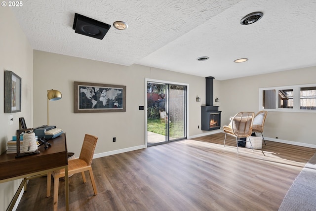 office featuring wood-type flooring, a wood stove, and a textured ceiling