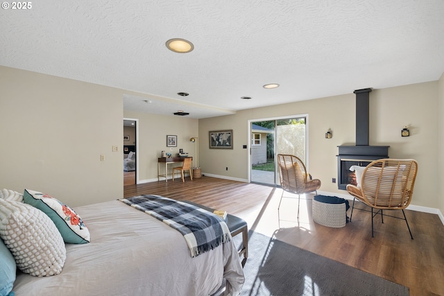 bedroom featuring a textured ceiling, access to outside, wood-type flooring, and a wood stove