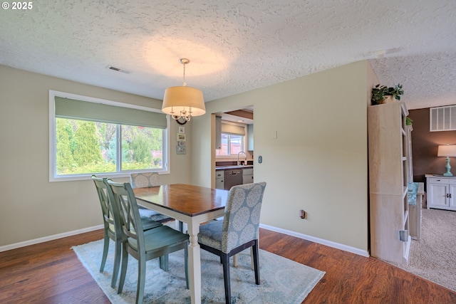 dining room featuring a textured ceiling, visible vents, baseboards, and wood finished floors