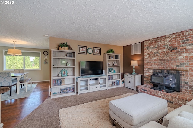 living room with visible vents, a wood stove, wood finished floors, baseboards, and a textured ceiling