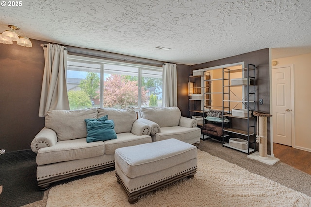 living room with a textured ceiling, visible vents, baseboards, and wood finished floors
