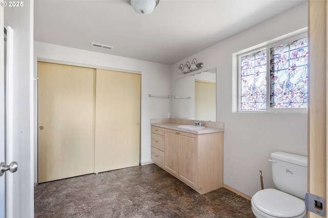 bathroom featuring visible vents, baseboards, toilet, stone finish floor, and vanity