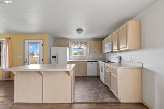 kitchen featuring white appliances, a center island, light countertops, a sink, and light brown cabinets