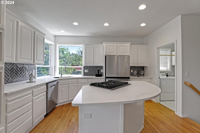 kitchen featuring light hardwood / wood-style flooring, appliances with stainless steel finishes, a center island, white cabinets, and washer / clothes dryer