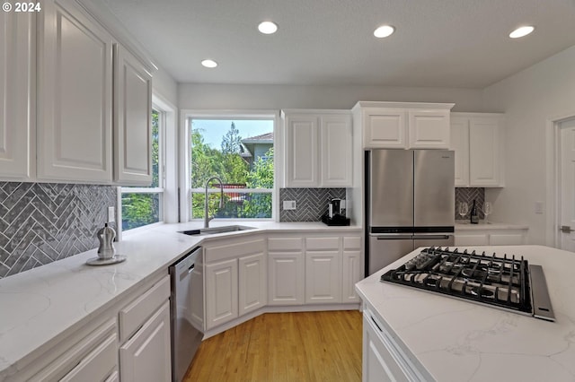 kitchen with sink, appliances with stainless steel finishes, white cabinetry, light stone counters, and light hardwood / wood-style floors