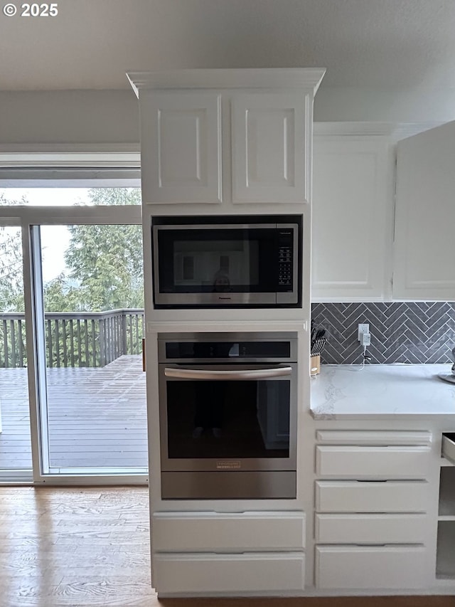 kitchen with white cabinetry, appliances with stainless steel finishes, decorative backsplash, and light hardwood / wood-style flooring