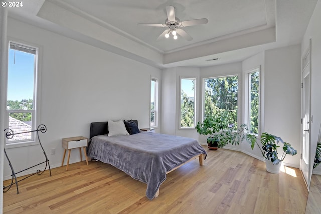 bedroom with light wood-type flooring and a tray ceiling