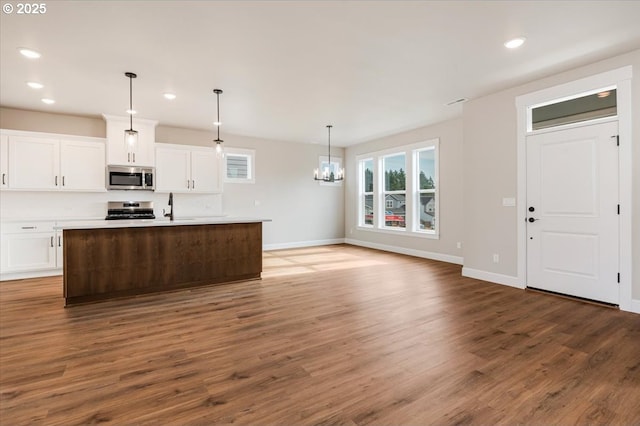 kitchen featuring sink, appliances with stainless steel finishes, a kitchen island with sink, hanging light fixtures, and white cabinets