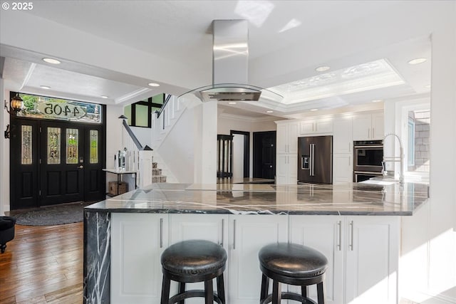 kitchen featuring high end black fridge, dark wood-style flooring, island range hood, crown molding, and white cabinetry