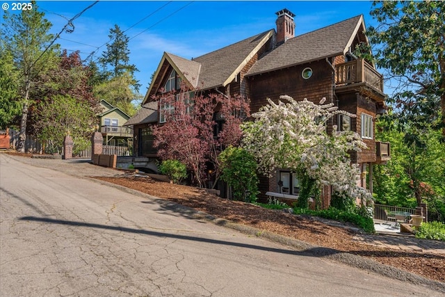 view of side of home featuring fence, a chimney, roof with shingles, and a balcony