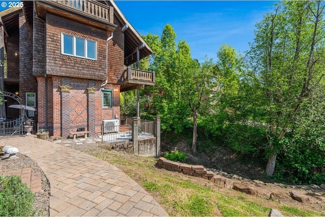 back of house with brick siding, fence, and a balcony