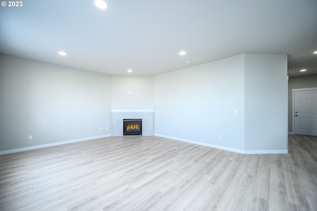 unfurnished living room with baseboards, a tile fireplace, light wood-style flooring, and recessed lighting