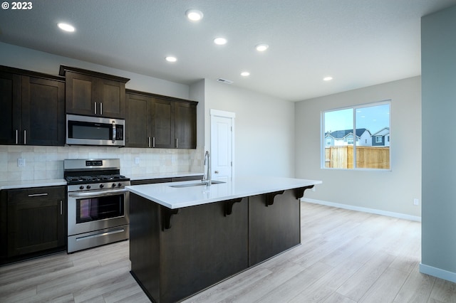 kitchen featuring appliances with stainless steel finishes, a kitchen breakfast bar, a kitchen island with sink, light countertops, and a sink
