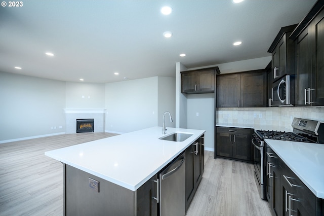 kitchen with a center island with sink, open floor plan, stainless steel appliances, light countertops, and a sink