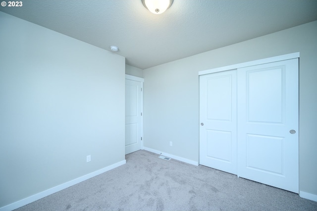 unfurnished bedroom featuring light carpet, a textured ceiling, baseboards, and a closet