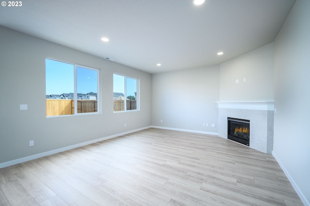 unfurnished living room featuring baseboards, light wood finished floors, a tile fireplace, and recessed lighting