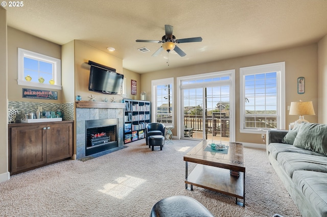 living room featuring visible vents, a textured ceiling, carpet, a fireplace, and ceiling fan