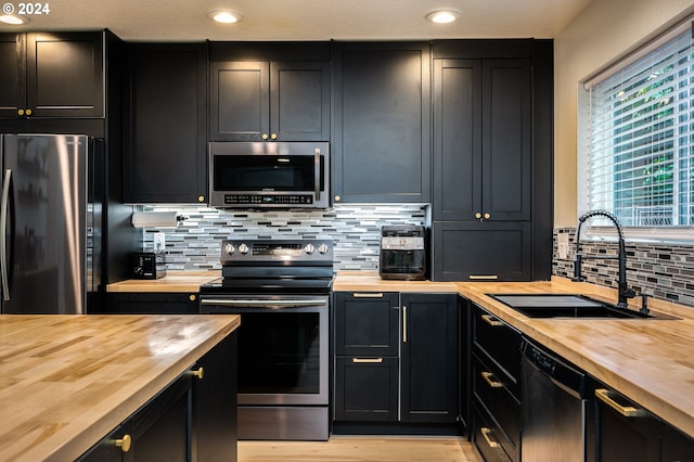 kitchen with decorative backsplash, appliances with stainless steel finishes, butcher block counters, and sink