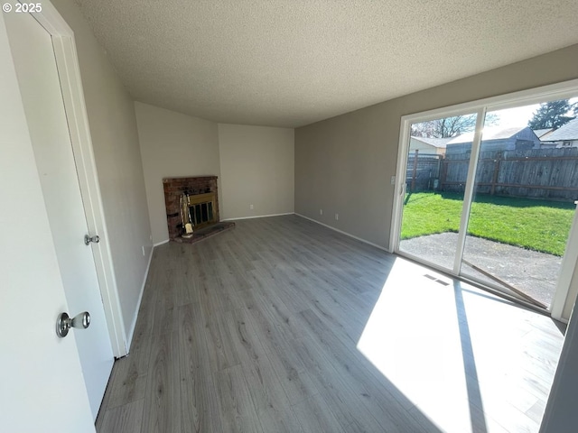 unfurnished living room with a textured ceiling, a brick fireplace, wood finished floors, and visible vents