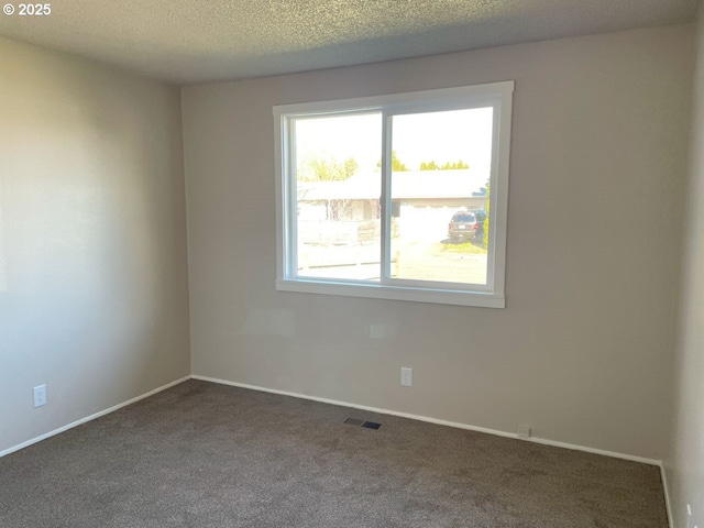 unfurnished room featuring visible vents, dark carpet, a textured ceiling, and baseboards