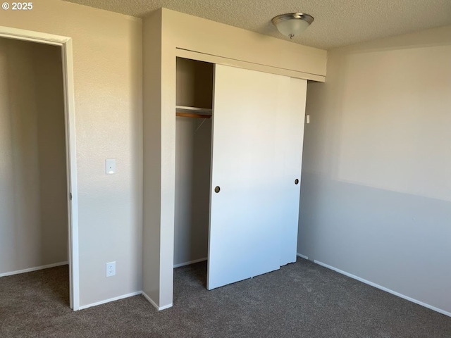 unfurnished bedroom featuring a textured ceiling, dark colored carpet, a closet, and baseboards