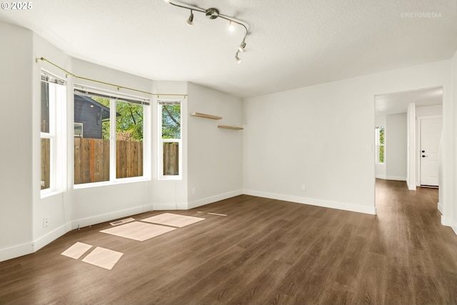 unfurnished room featuring baseboards, a wealth of natural light, and dark wood-type flooring