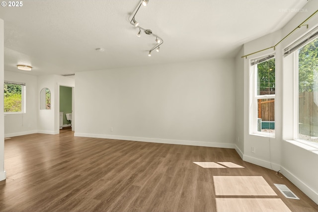 unfurnished room with visible vents, baseboards, wood finished floors, and track lighting