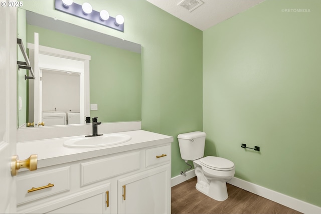 half bathroom featuring vanity, toilet, baseboards, wood finished floors, and visible vents