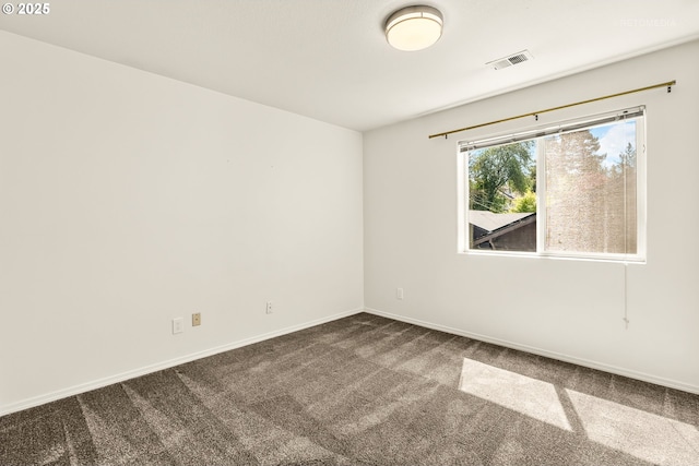 spare room featuring dark colored carpet, baseboards, and visible vents