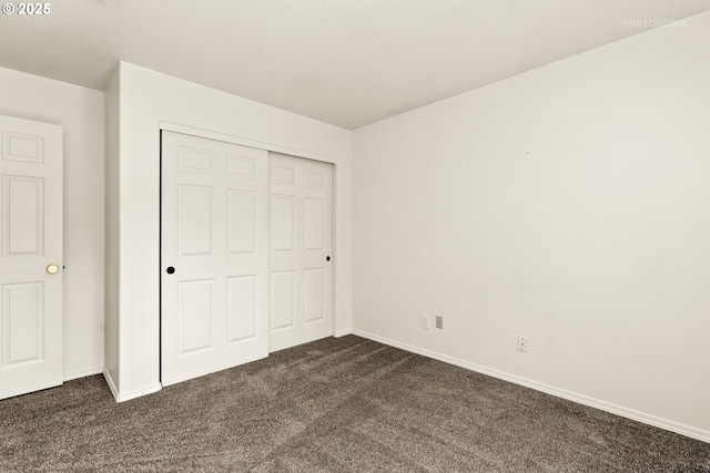 unfurnished bedroom featuring dark carpet, baseboards, and a closet