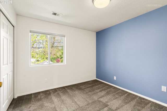 unfurnished bedroom featuring baseboards, a closet, dark colored carpet, and visible vents