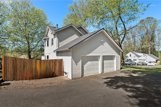 view of home's exterior featuring an attached garage, fence, roof with shingles, and aphalt driveway