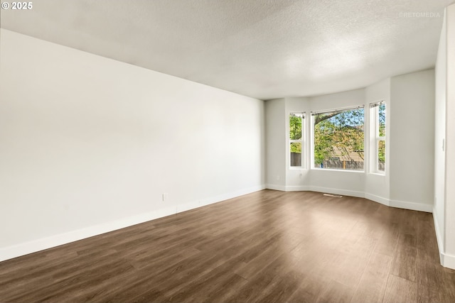 spare room featuring baseboards, dark wood-style flooring, a textured ceiling, and visible vents