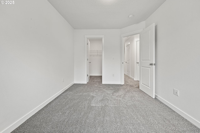 unfurnished bedroom with light colored carpet, a closet, a textured ceiling, and a walk in closet