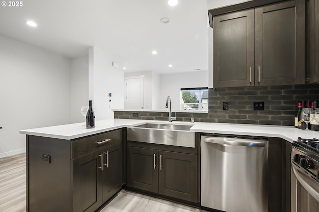 kitchen with sink, backsplash, kitchen peninsula, stainless steel appliances, and light hardwood / wood-style flooring