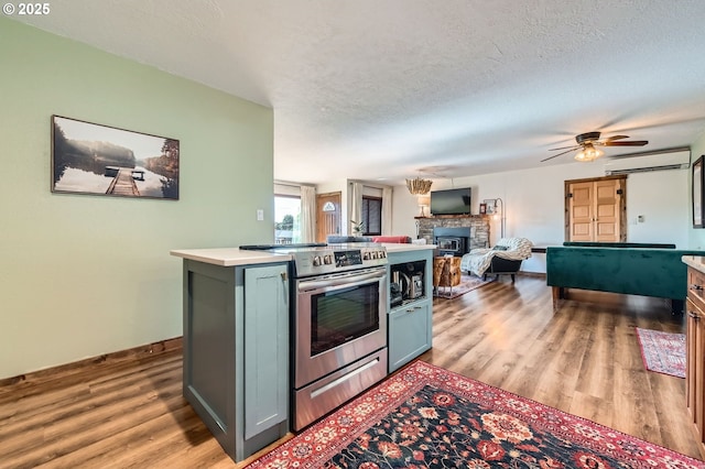 190 SE Shafford St, Estacada, OR 97023 - kitchen with stainless steel electric stove, light wood-style flooring, a fireplace, a wall mounted AC, and ceiling fan