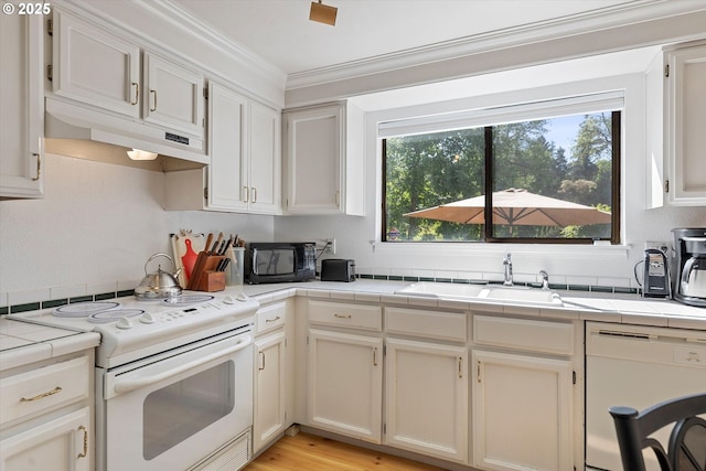 kitchen featuring white appliances, tile counters, under cabinet range hood, a sink, and plenty of natural light
