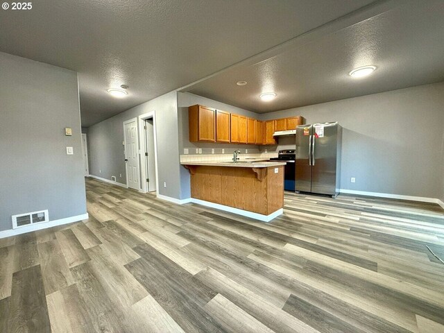 301 SE 129th Ave, Portland, OR 97233 - kitchen featuring stainless steel appliances, baseboards, a peninsula, under cabinet range hood, and light wood-style flooring