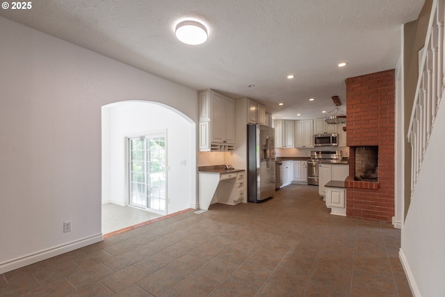 7105 Mississippi Dr, Vancouver, WA 98664 - kitchen featuring stainless steel appliances, dark countertops, arched walkways, a brick fireplace, and recessed lighting