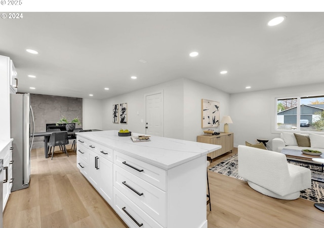 kitchen with light stone countertops, a kitchen island, stainless steel fridge, light hardwood / wood-style floors, and white cabinets