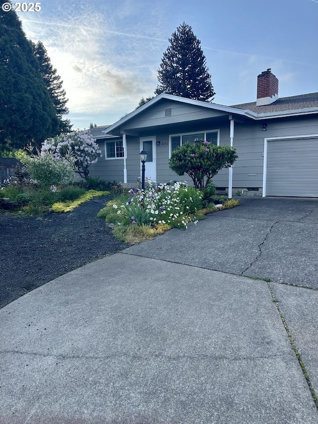 ranch-style home featuring driveway, a chimney, and an attached garage